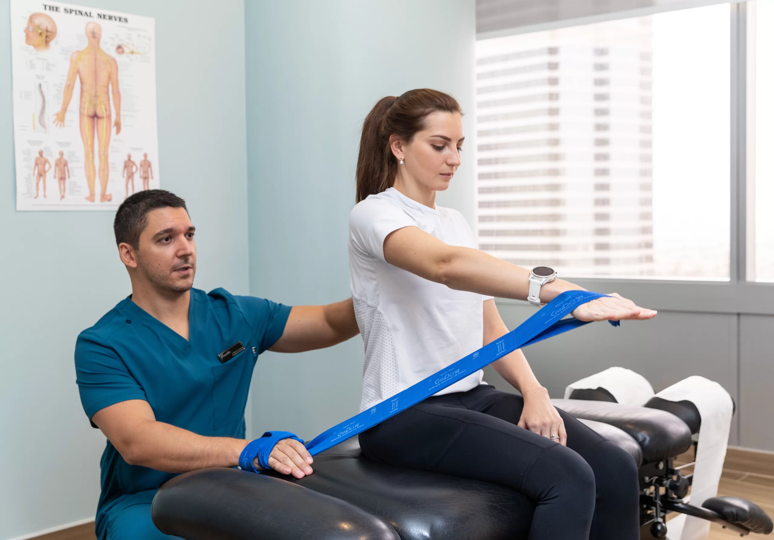 Physiotherapist at a physiotherapy center in Dubai guiding a female client with resistance band exercises, her arm slightly lowered for controlled movement.