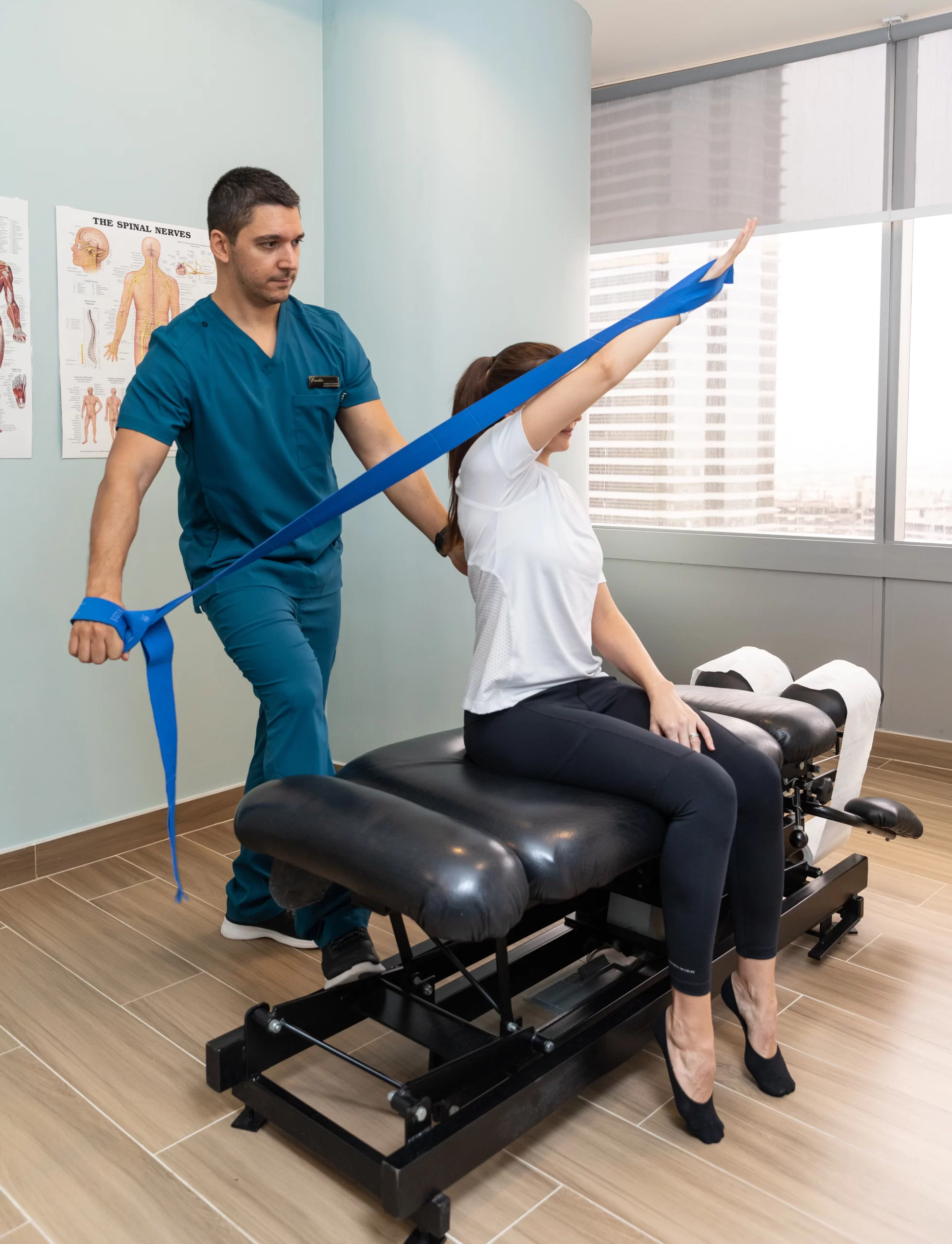 Physiotherapist at a physiotherapy clinic in Dubai assisting a female client with a resistance band exercise, her arm pointing to the ceiling for a shoulder stretch.