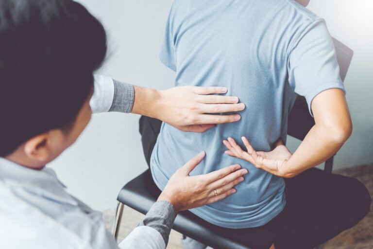 Chiropractor assessing a seated patient's lower back during a sciatica assessment